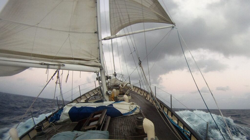 El velero parece despegar del mar al subir su proa en una ola.