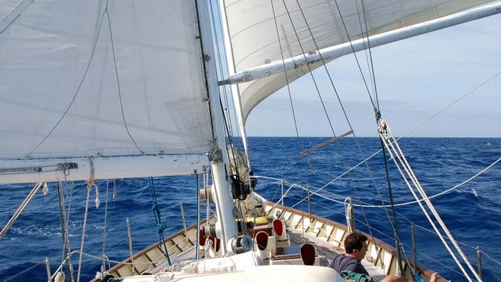 Velas desplegadas, una a cada lado navegando viento en popa con el azul del océano alrededor