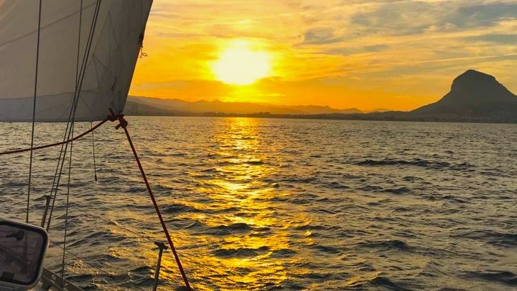 Puesta de sol con monte Montgó a la derecha y vela de proa a la izquierda, durante prácticas de habilitación a Baleares