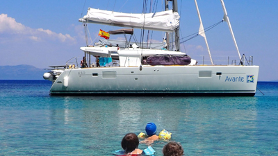 Curso PER presencial: Barco fondeado en aguas turquesas con niños nadando hacia el barco