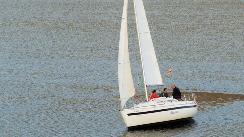 Un velero blanco navega sobre aguas grisáceas en prácticas de vela