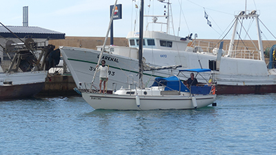 Pareja navegando en pequeño velero acercándose al puerto